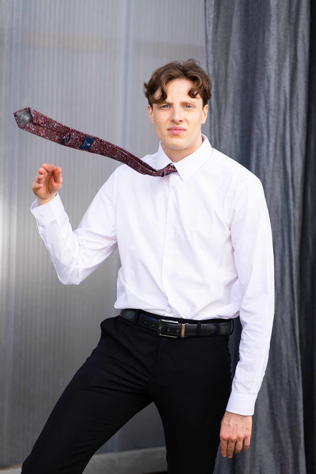 Junger Schauspieler mit weißem Hemd und schwarzer Hose und fliegender Krawatte. Sedcard Shooting in München. Schauspieler fotografiert münchen.