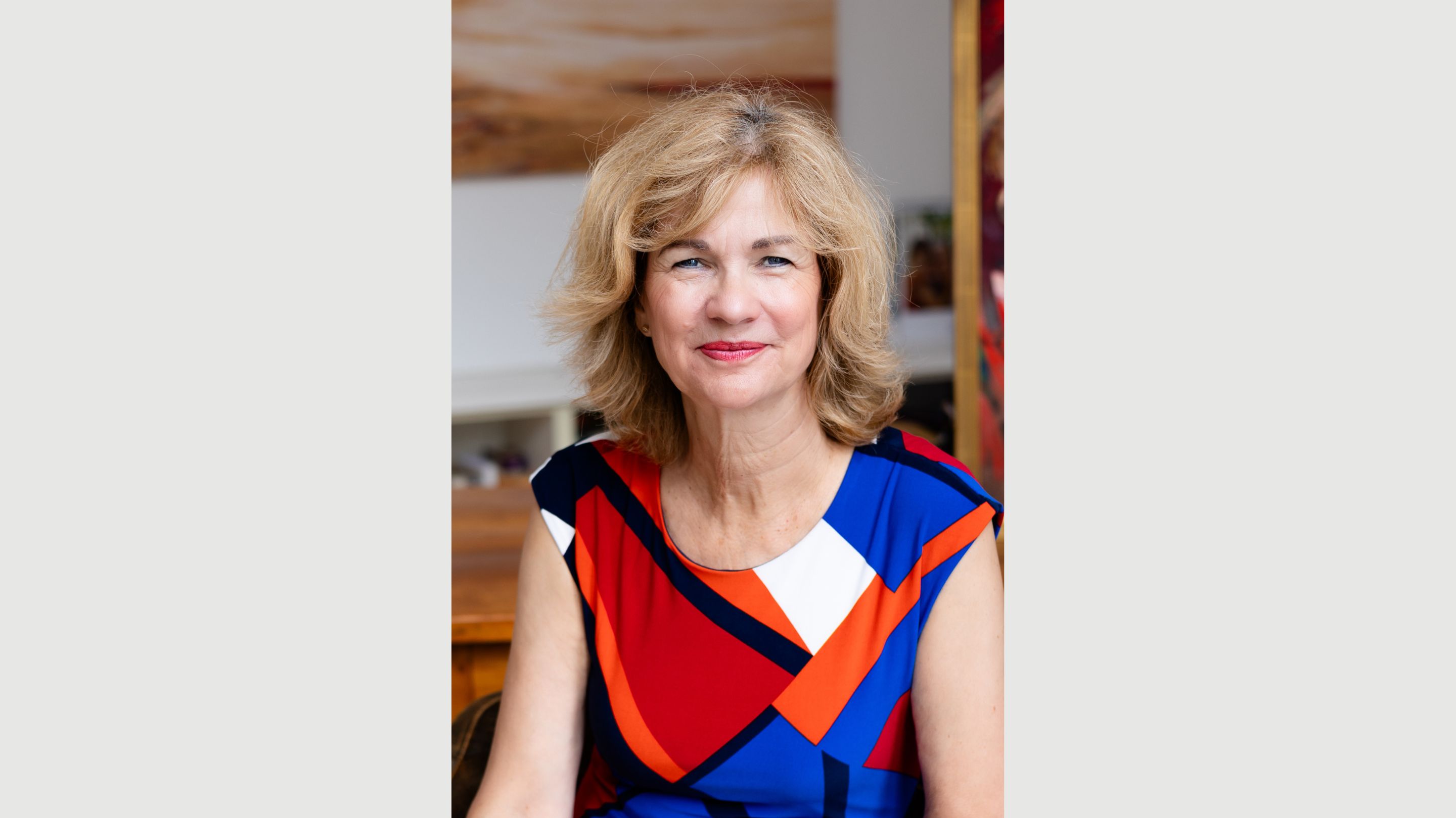 Nahes Personal Branding Portrait von Ilona Libal in ihrer Wohnung. Sie trägt ein farbenfrohes Kleid in Rot, Blau und Orange und blickt ruhig und offen in die Kamera.