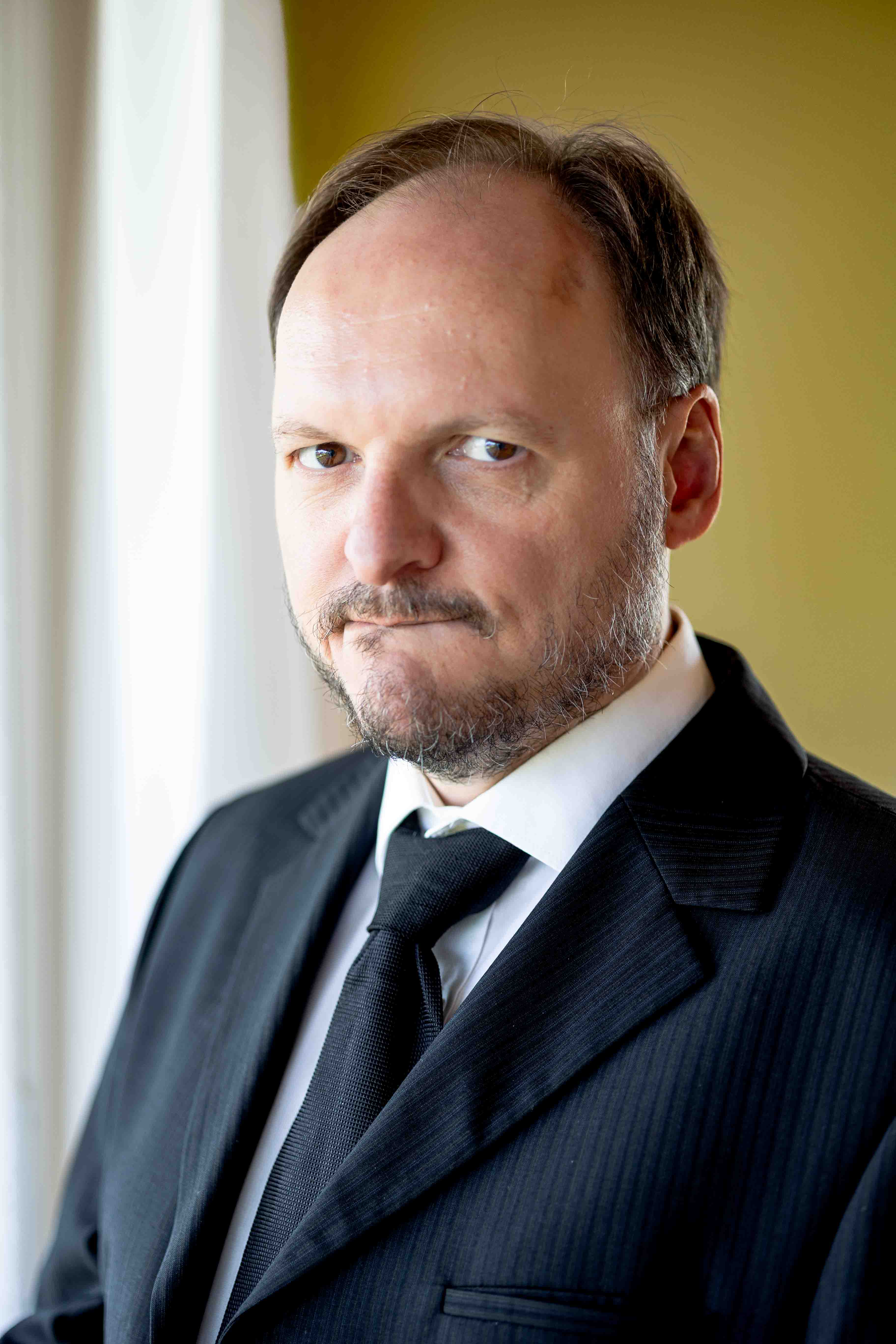Schauspieler Mike Sobotka im schwarzen Anzug vor einem Fenster